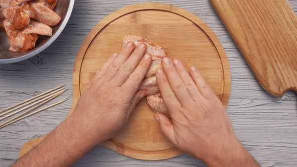 Hands are Placing Chicken Wings on a Board and Piercing It with a Wooden Skewer alt