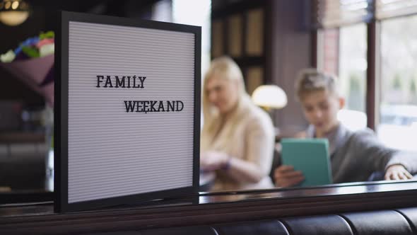 Closeup Family Dinner Announcement in Cafe with Blurred Mother and Son Sitting at Table at alt