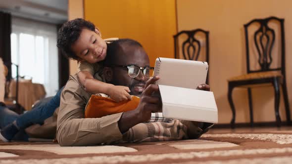 Biracial boy laying on his father's back and watching on tablet computer