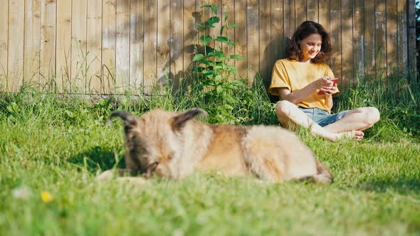 Young Woman Uses Her Smartphone Leaning Her Back Against the Wooden Wall alt