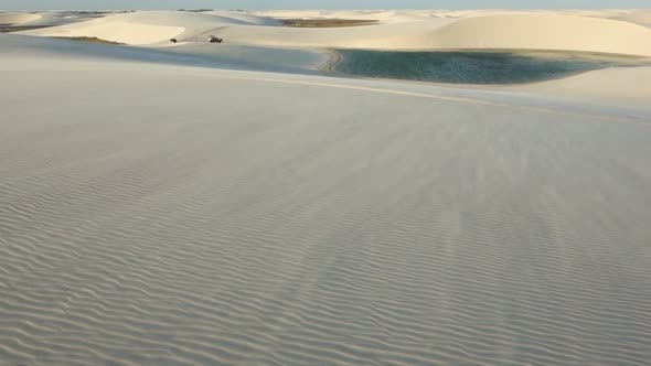 wind blowing over textured dunes, carrying off sand. oasis lagoon on backgroung. desert landscape alt