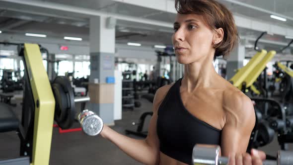 Sporty Mature Woman is Making Biceps Exercise with Dumbbells in Gym alt