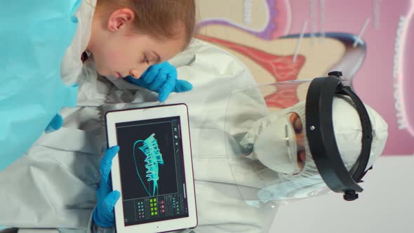 Vertical Video Dentist with Ppe Suit Pointing on Digital Screen Explaining Xray to Mother alt
