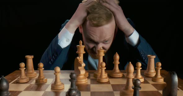 Businessman in Black Suit Is Sitting in Front of Chessboard with Stressed Face Expression alt