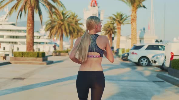 Blonde Woman with Tail Jogging Along the Alley with Palm Trees