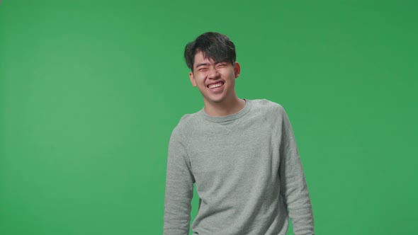 A Smiling Asian Man Dabbing While Standing In Front Of Green Screen Background alt