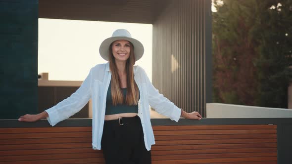 Pleasant Female Traveler in Stylish Hat and Outfit Leaning on Wooden Fence and alt