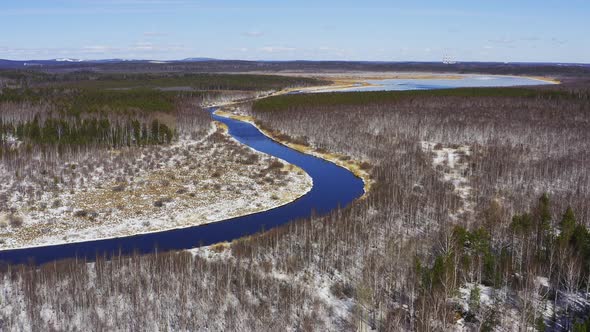 Aerial Footage the River Flows in The Forest Among the Snowy Shores in Sunny Weather alt