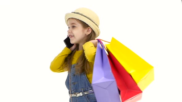 Little Girl Holding Bags and Talking on the Phone, Smiling. White Background. Slow Motion alt