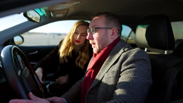 Side View of Wealthy Stylish Caucasian Man Sitting on Driver's Seat in Car with Blurred Confident alt
