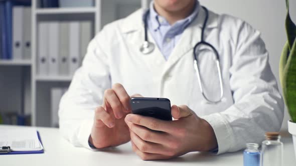 Doctor Is Working, Looking For Information, Chatting With Patient On Mobile Phone In Office alt
