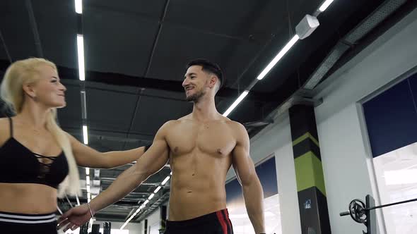 Confident Guy with Nake Torso and Attractive Woman Walking in Gym alt