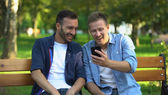 Best Male Friends Looking Through Photos on Smartphone, Having Fun at Park alt