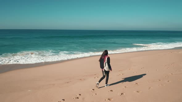 Young brunette woman walking along the Atlantic ocean coastline, enjoying a view of crashing waves
