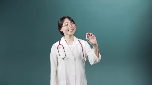 An Attractive Young Doctor Smiles and Shows an Ampule with Vaccine alt
