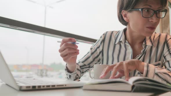 Serious Business Woman in Eyeglasses Works with Laptop and Paper Organiser in Coworking Center alt