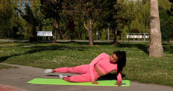 Beautiful slim young woman sitting on yoga mat on sunny day and stretching.