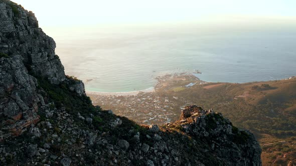 Aerial shot flying over the mountain's edge to reveal Camp's bay and the ocean