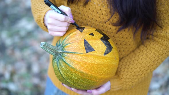 Close Up Woman Hands Paint Orange Pumpkin with Black Paint in Autumn Forest