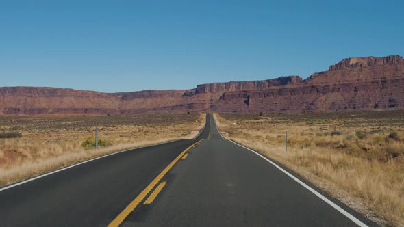 Driving On An Empty Road Leading To Red Mountain Rocks And Hills alt