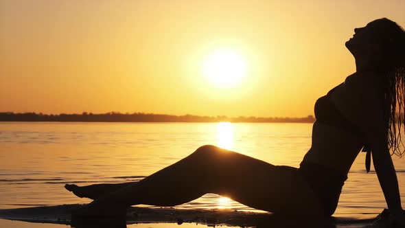Silhouette of Hot Woman in Swimsuit Lying and Posing on Evening Beach at Sunset alt