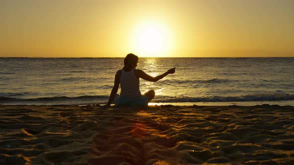 Silhouette of Woman Sitting on Golden Sand at Sunset Sand Through Fingers alt