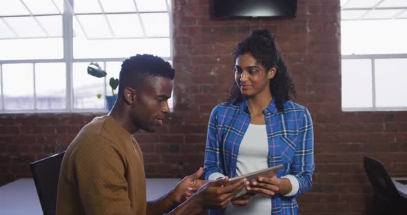 Diverse female and male business colleagues in discussion at work looking at digital tablet alt