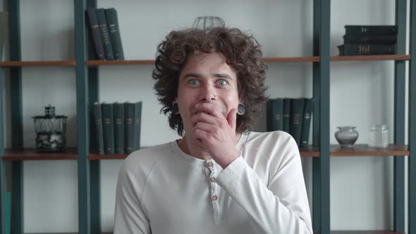 Amazed Curlyhaired Guy with Tunnels in His Ears Looking at Camera and Saying WOW alt
