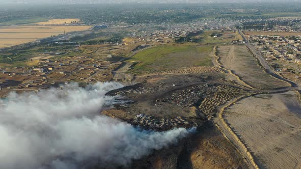 Aerial view of burning garbage pile in trash landfill polluting city with smoke alt