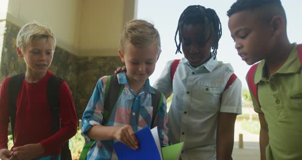 Video of happy diverse boys walking, looking at notebook in front of school alt