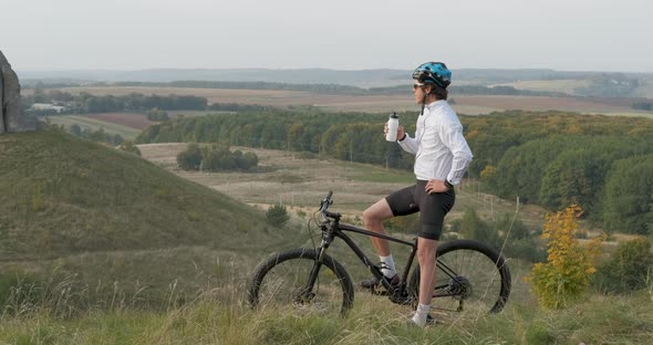 Professional Cyclist Makes Stop to Drink Water on the Hill with Beautiful View