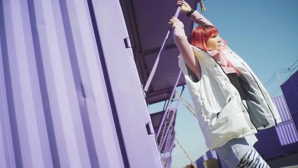 Portrait of Independent Young Woman with Pink Hair Posing on Purple Containers Background alt