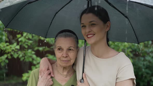 Old and Young Women Under Umbrella in the Rain alt