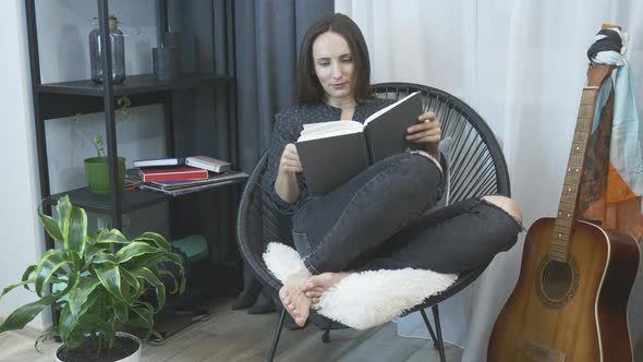 Young woman sitting on cozy chair, relaxing and reading book. Relaxation at home. alt
