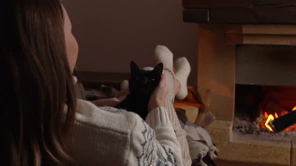 Woman Hands Pet Cute Black Cat Sleeping in Her Lap in Front of Fireplace alt