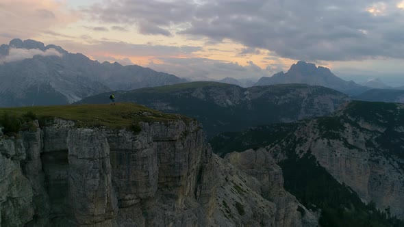 Aerial view push towards hikers trekking on grass topped Tre Cime mountain range early sunrise scene alt