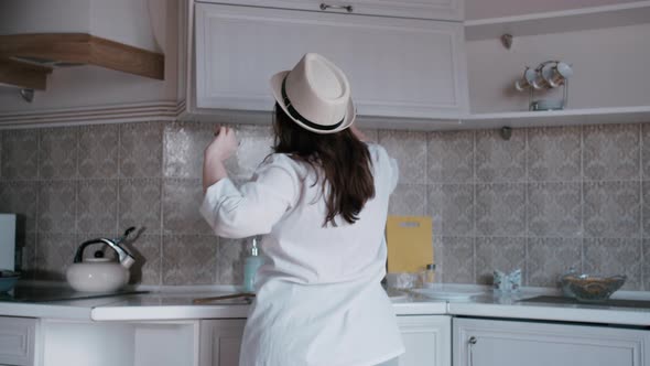 Happy Overweight Woman in a Hat Cooks in the Kitchen and Dances Good Mood Cooking in the Evening at