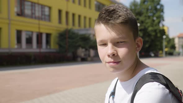 A Caucasian Teenage Boy Smiles at the Camera  Closeup  a School in the Background