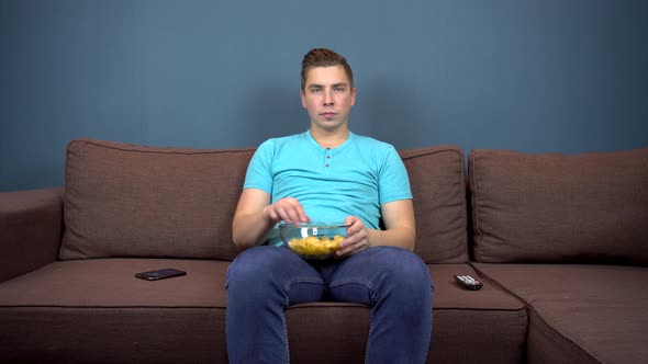 A Young Man Sits on a Sofa Eating Chips and Watching TV, The View From the TV, Looking at the Camera alt