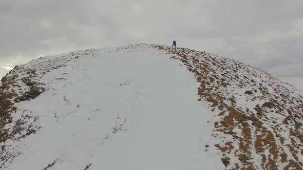 Aerial view of a trail runner running to the top of a snowy mountain alt