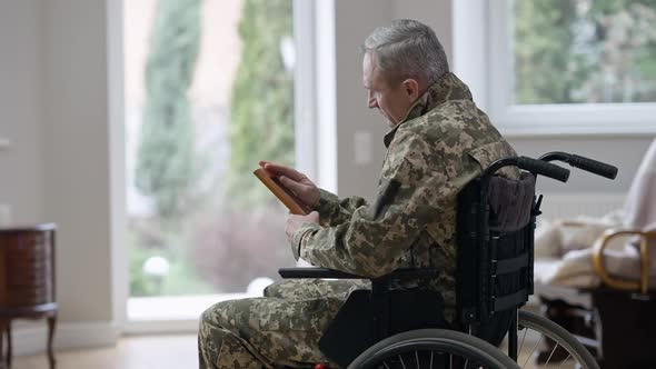 Side View of Frustrated Middle Aged Man in Wheelchair Looking at Picture and Crying alt