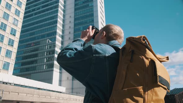 A Male Traveler with a Yellow Backpack Takes Pictures of the City on Camera alt
