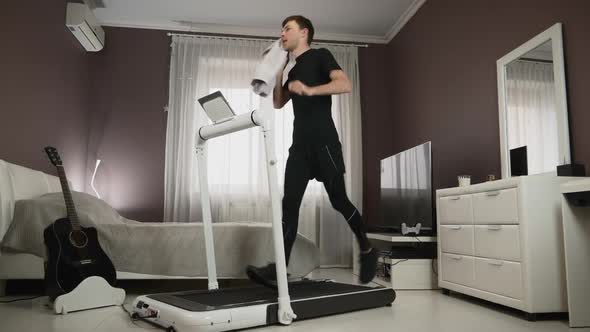Man is wiping his face with towel during running on treadmill alt