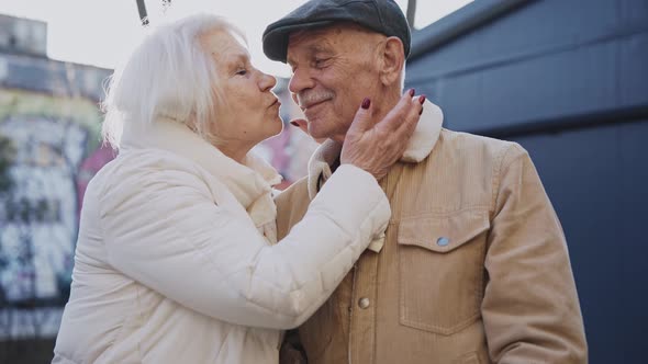 A Stylish Elderly Couple Kiss Standing on a Sunny Modern Street