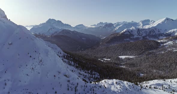 Backward Aerial to Snowy Alpine Valley with Woods Forest at Valparola Pass