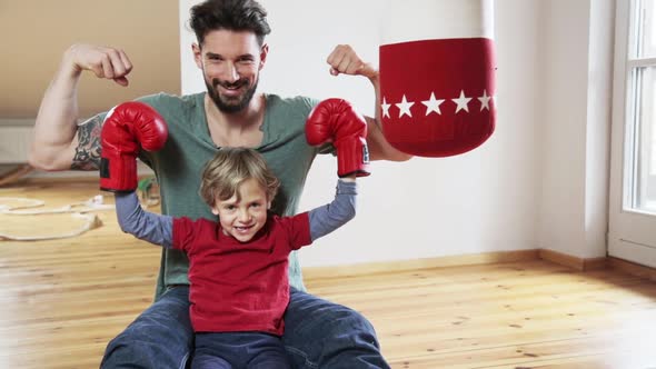 Father holding up his sons arms with boxing gloves