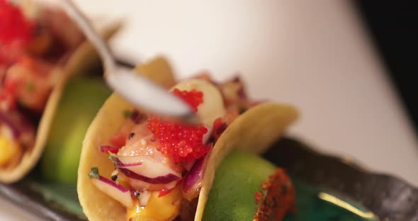 Chef In The Kitchen Putting Red Caviars On Top Of Sushi Tacos Using A Teaspoon. - close up shot alt