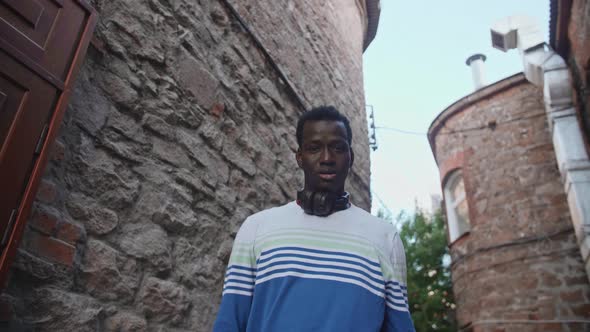 A Young Black Student with Headphones Walks Through the City Centre at Sunset