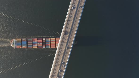 The Container Ship Passes Under a Large Bridge Over Which Cars are Moving alt