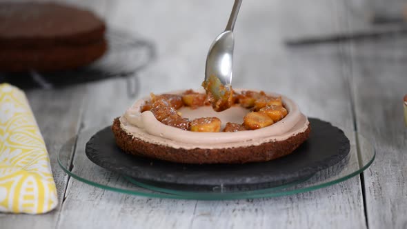 A confectioner puts caramelized bananas on a cake. Process of cooking chocolate sponge cake.	 alt
